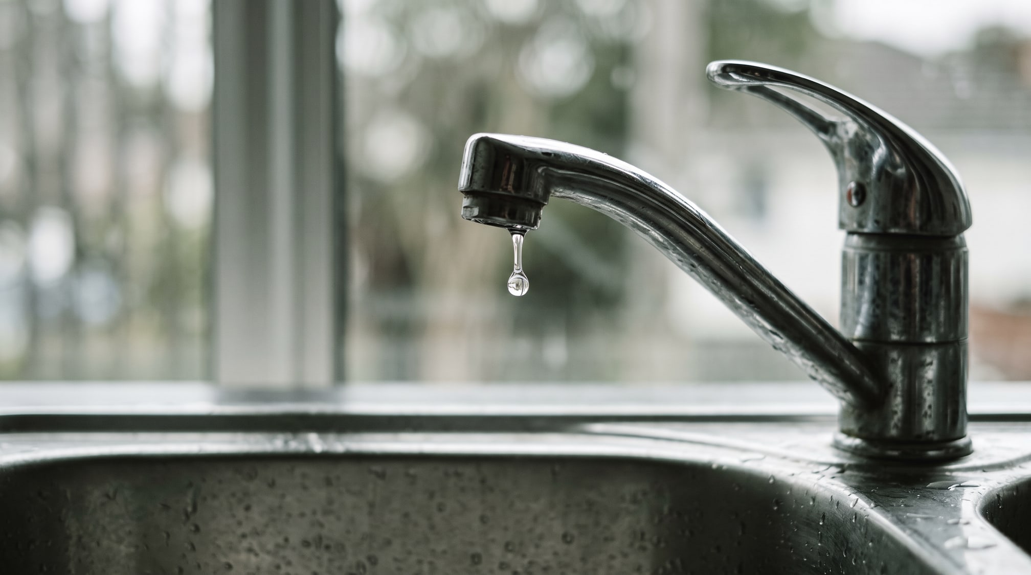 Gros plan d'un robinet de cuisine dont une goutte se forme au bec